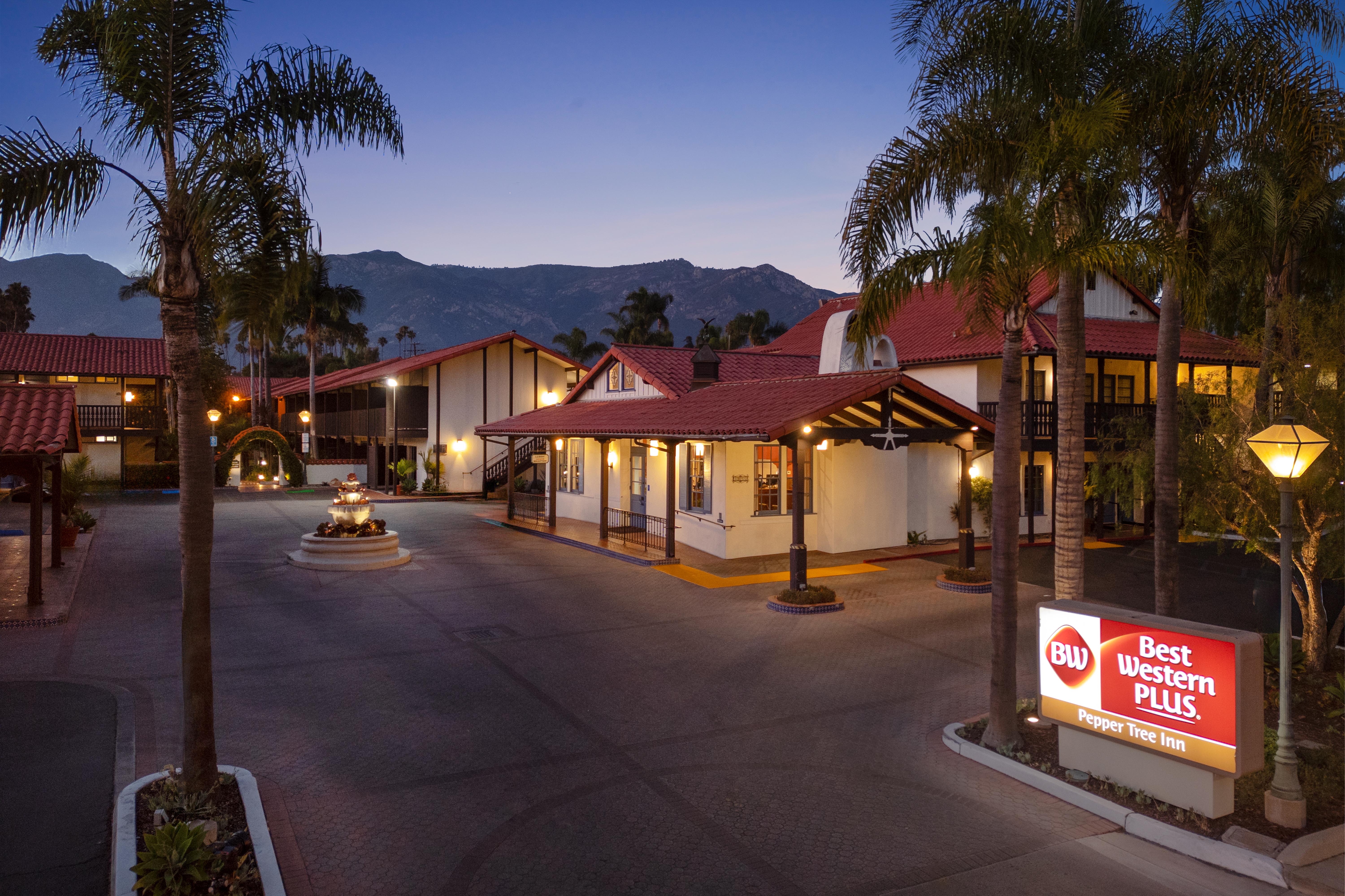 Exterior view of Best Western Pepper Tree Inn with courtyard, palm trees, and lit buildings at dusk